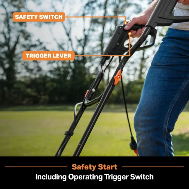 Person holding black push mower with labeled safety switch and trigger lever in a grassy yard.