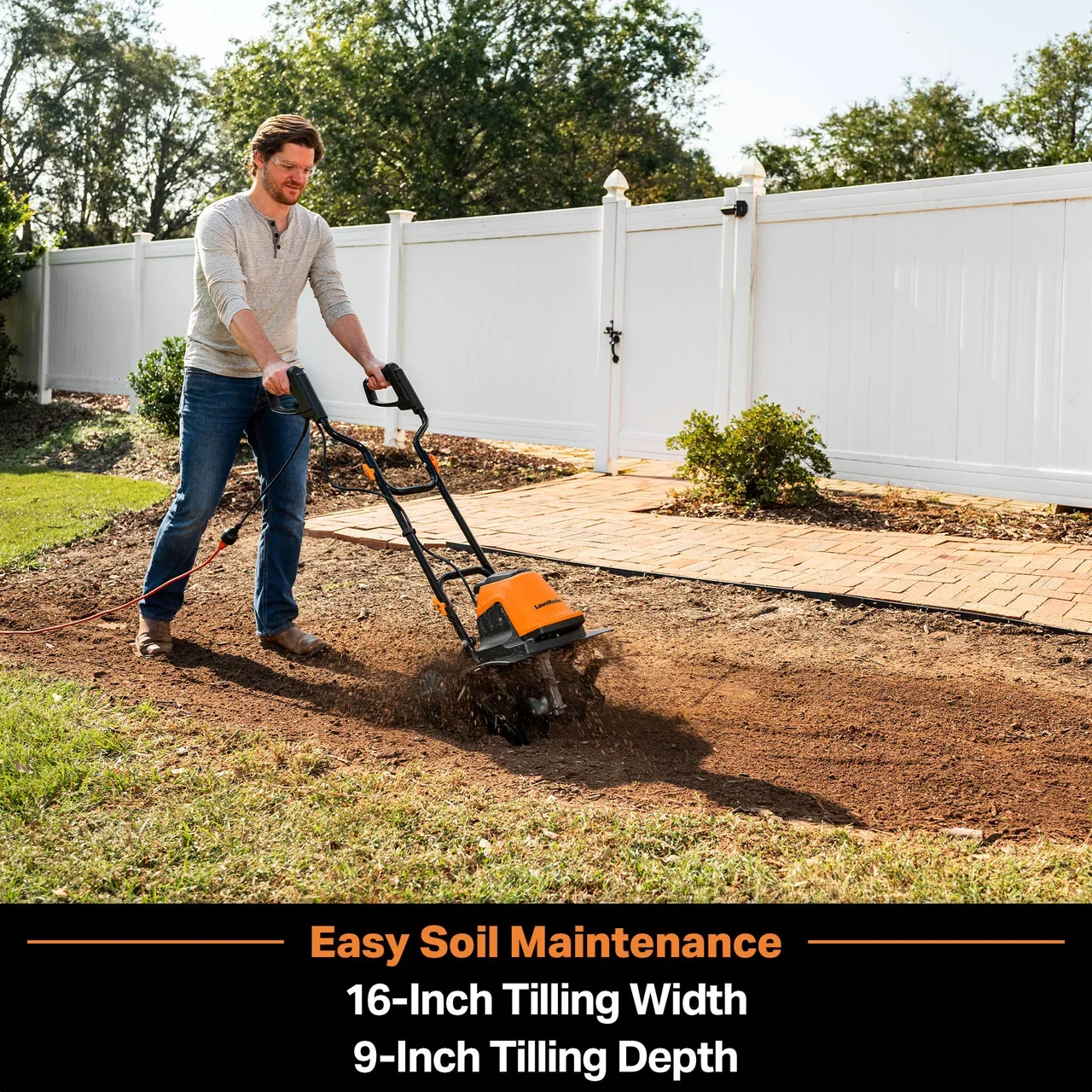 Man operating a front-tine tiller with 16-inch width and 9-inch depth to maintain garden soil near a white vinyl fence.