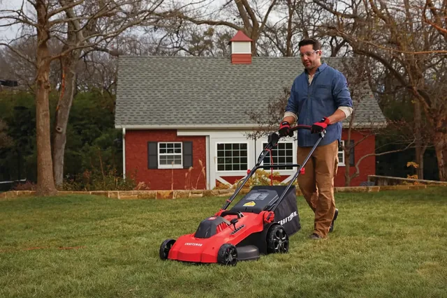 Photo of CRAFTSMAN lawn mower CMEMW213 in use on grass by a person, with a red brick house in the background.
